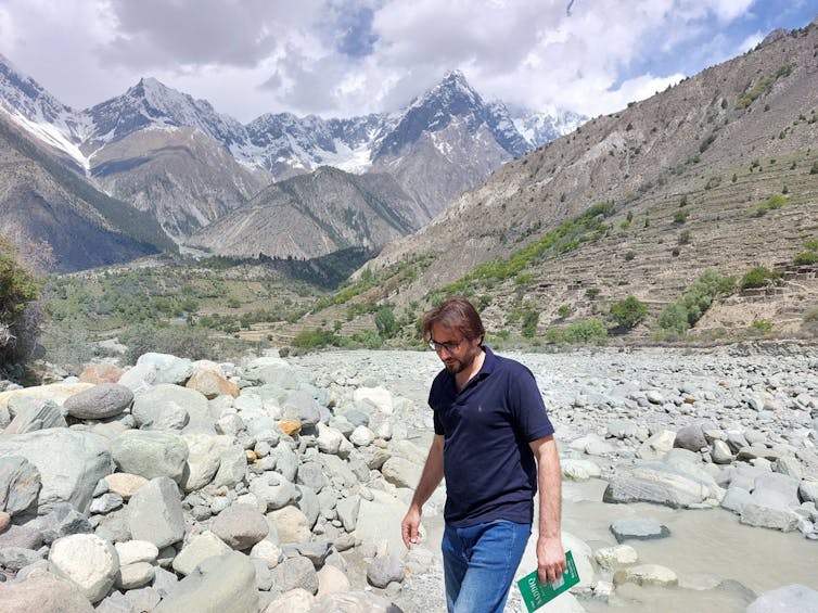 A man walks over some rocks with mountains in the background