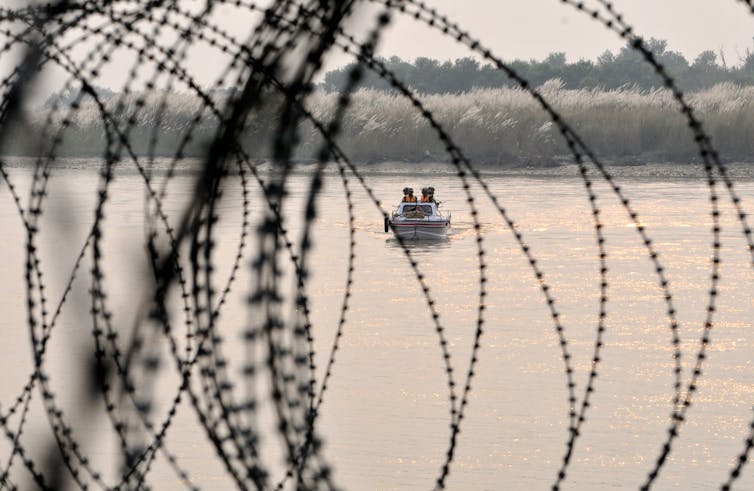 A boat floats on the water behind barbed wire