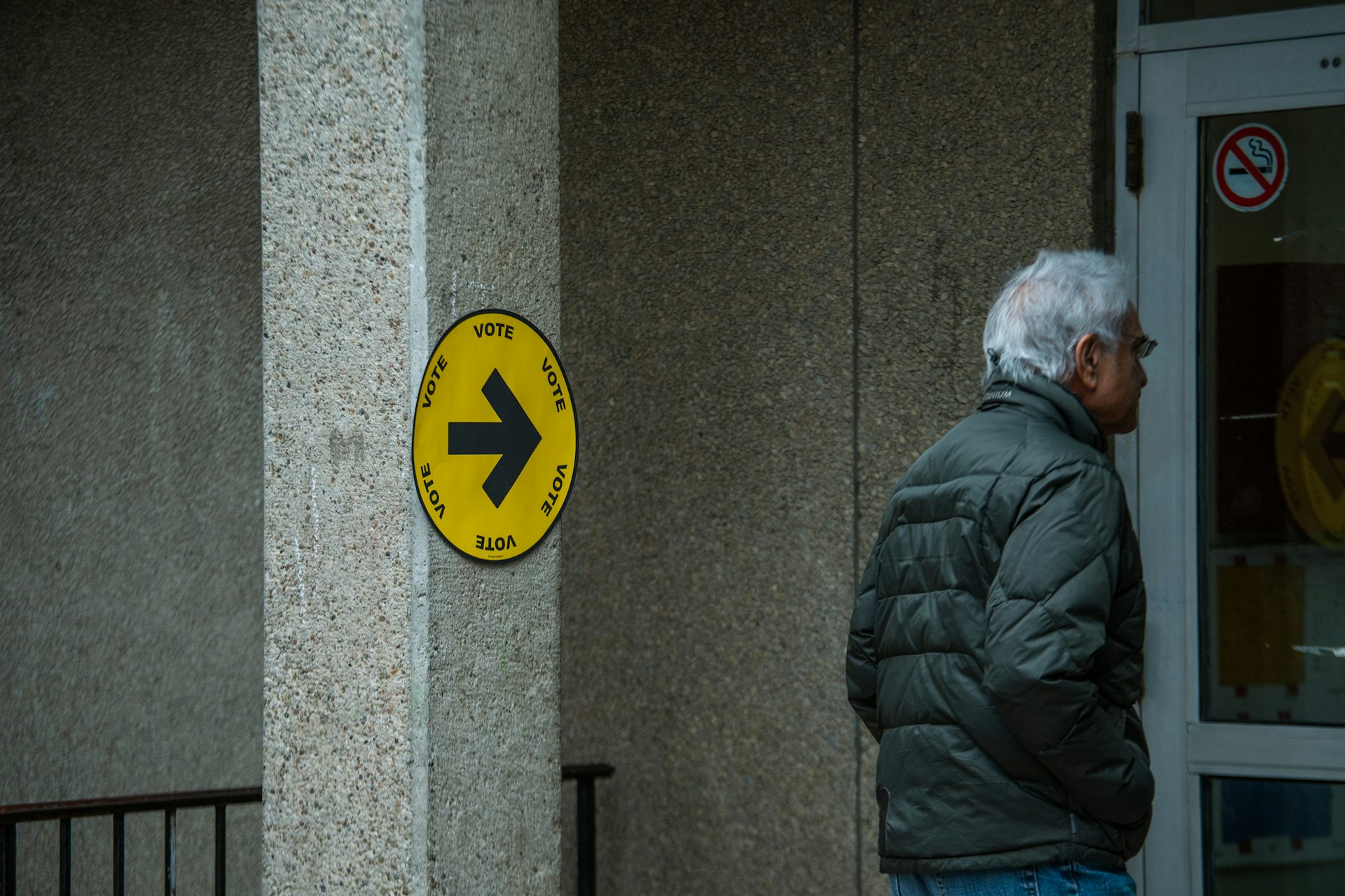 Hombre con cabello gris caminando hacia la entrada marcado con un signo amarillo 