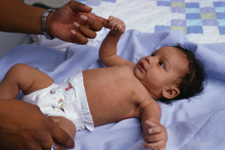 A baby girl grasps an adult's finger