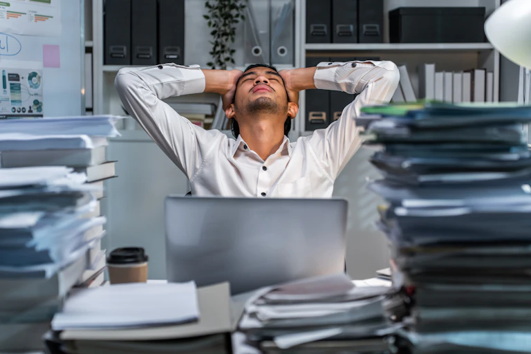 Man looking exhausted at busy work desk.