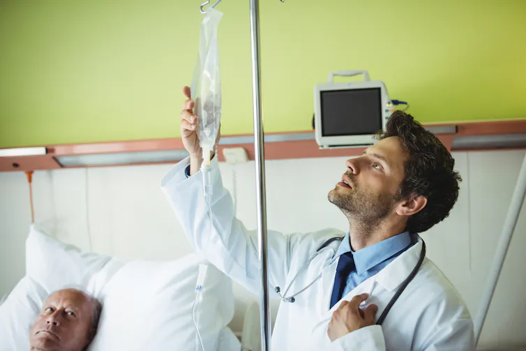 A doctor examining a drip. The patient looks on nervously.