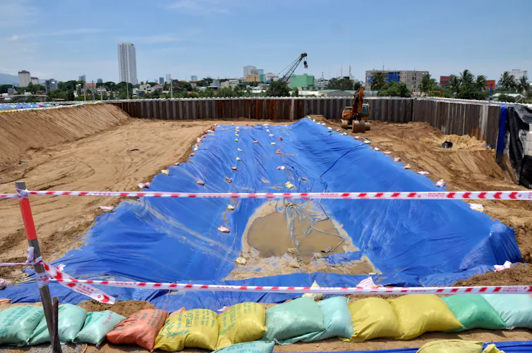 A pit with sandbags and tarps and buildings in the background.