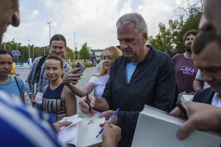 A man seen signing books surrounded by a crowd.