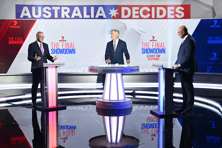 Journalist Mark Riley flanked by Anthony Albanese and Peter Dutton, who are standing at podiums beneath an 'Australia Decides' sign