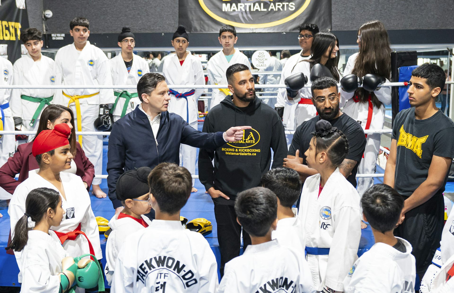 El hombre de cabello oscuro se encuentra entre otros hombres y en su mayoría niños en el estudio de artes marciales.