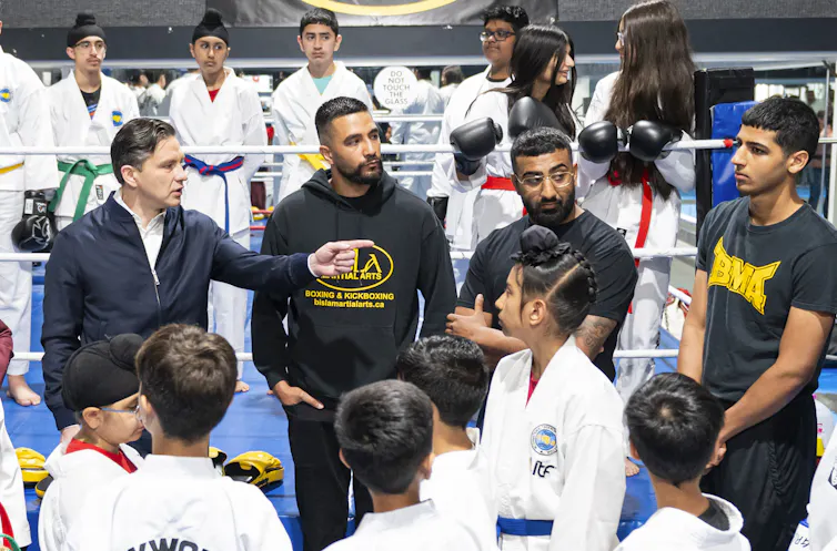 El hombre de cabello oscuro se encuentra entre otros hombres y en su mayoría niños en el estudio de artes marciales.