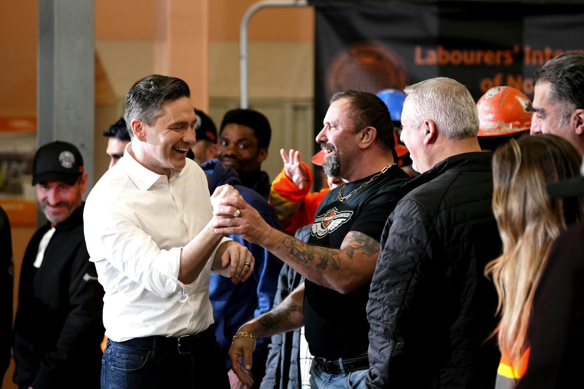 El hombre de cabello oscuro con un vestido de camisa blanca se maneja con otros hombres con camisetas.