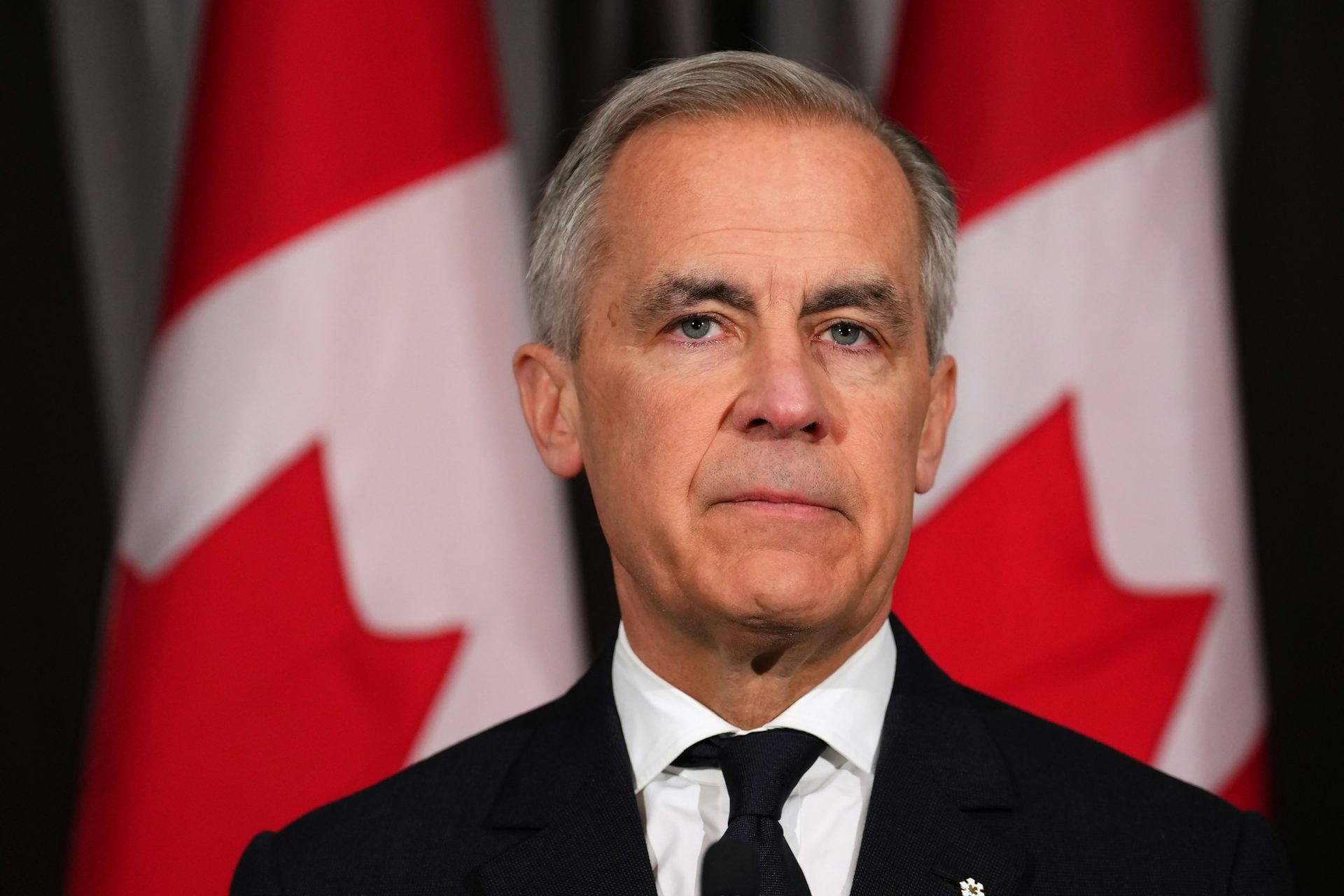 Un hombre con un cabello corto y oscuro se encuentra frente a la bandera canadiense.
