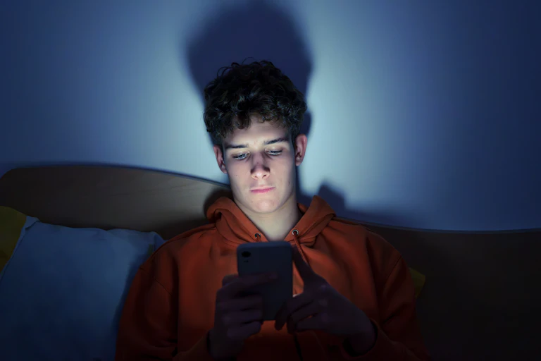 A young man stares into his phone in the dark