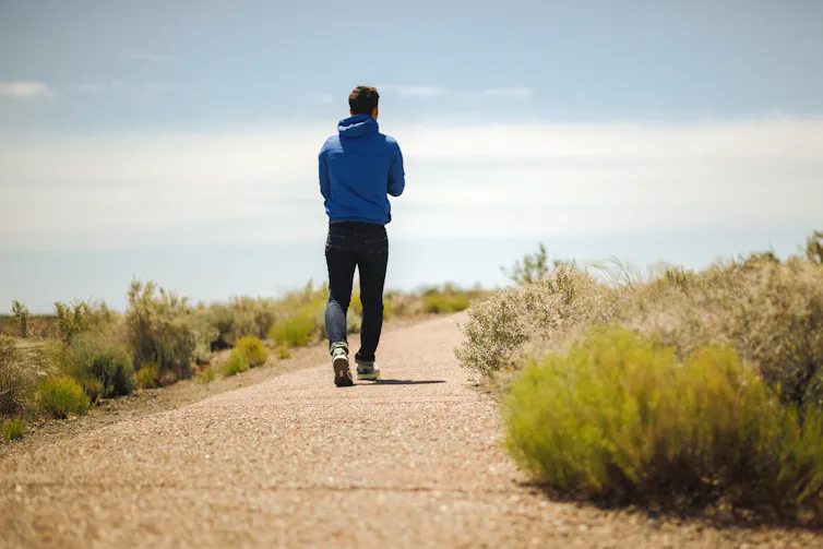 A man walking on a path outside on a sunny day.