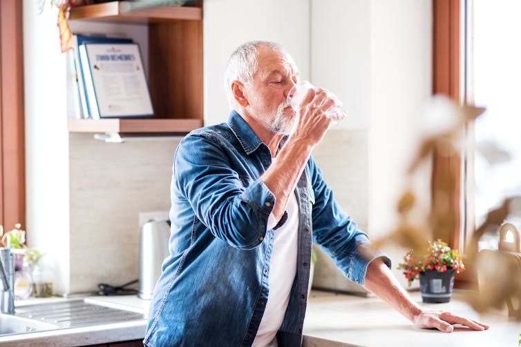 An old man is drinking a glass of water in the house.