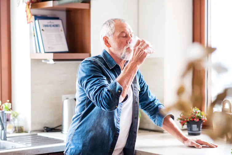 An older man drinking a glass of water at home.