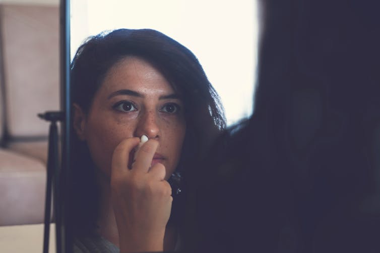 Woman looks in the mirror while spraying her nose