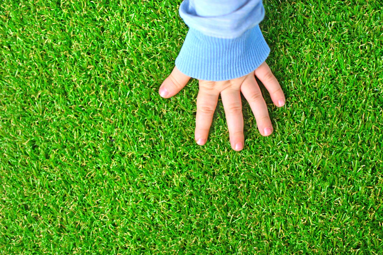 Tender hand of a baby on green artificial turf.