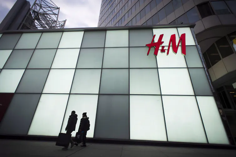 two people are silhouetted agains the façade of an H&M store
