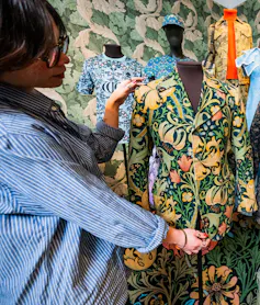 A woman standing by a tailor's dummy of a jacket in a William Morris pattern called 'Golden Lily'.