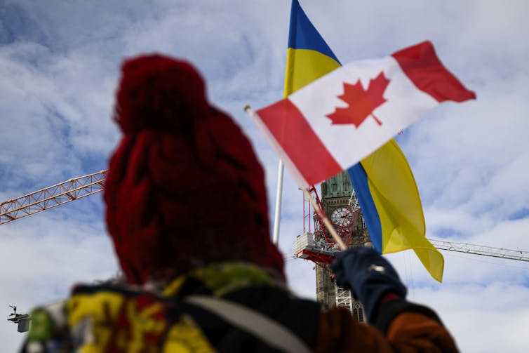 Una persona que agita la bandera canadiense contra la gran bandera ucraniana de otra persona.