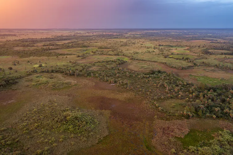 An orange, pink, purple and blue sky over large area of wetlands