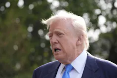 An elderly man with fluffy blond hair looks tired as he speaks to reporters outside.