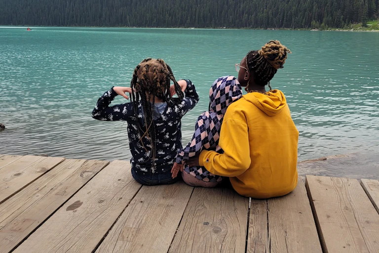 A parent sitting in front of mountain and lake with children.