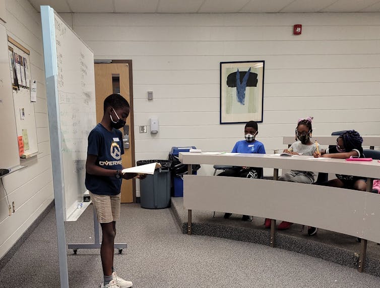 Un estudiante negro presentado en el aula en el frente mientras otros estudiantes que se enfrentaban a ellos escuchándolos.