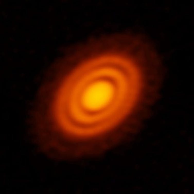 A protoplanetary disk in space, featuring a bright star in the center, reflecting yellow light, and surrounded by swirls of orange dust.