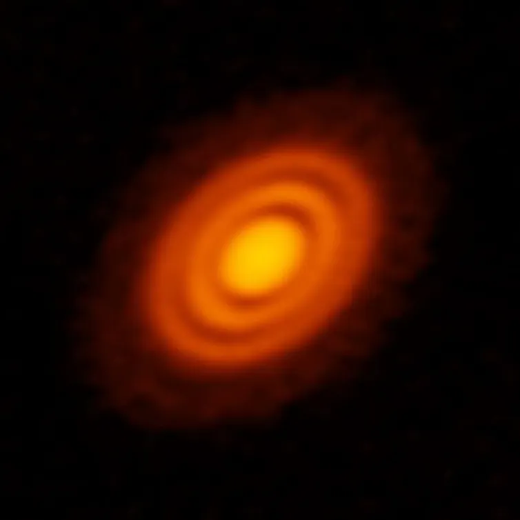 A protoplanetary disk in space, featuring a bright star in the center, reflecting yellow light, and surrounded by swirls of orange dust.