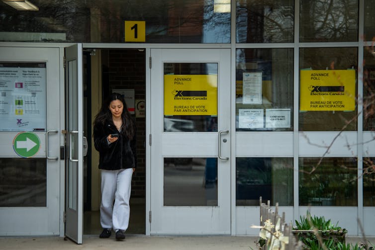 La mujer deja un edificio con una elección amarilla de CanadÔ que se recogen en las ventanas.