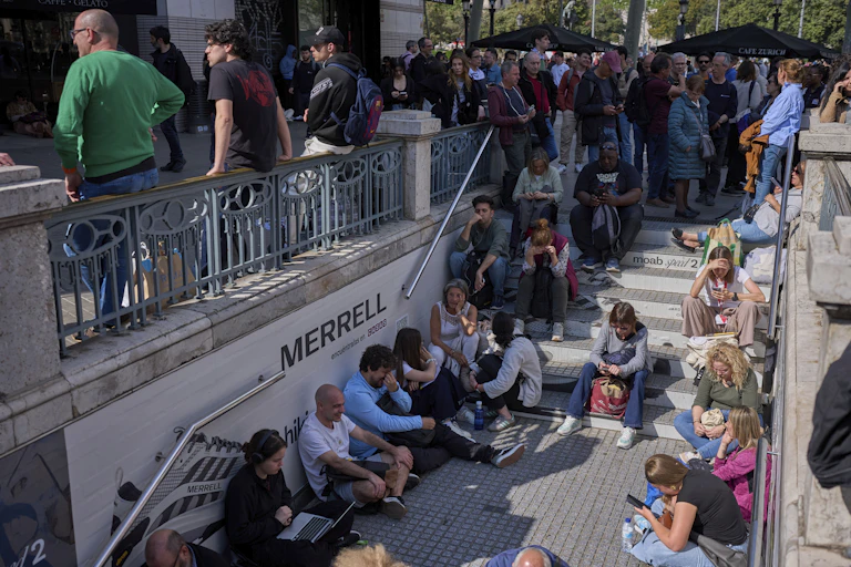 A large crowd of people sitting on and standing around a staircase leading to a subway.