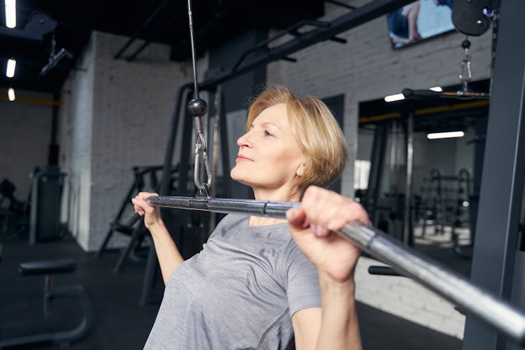 Mujer utilizando una máquina de jalón lateral en el gimnasi