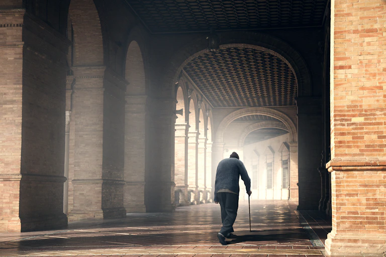 An older man with a hunchback walks down a passage.