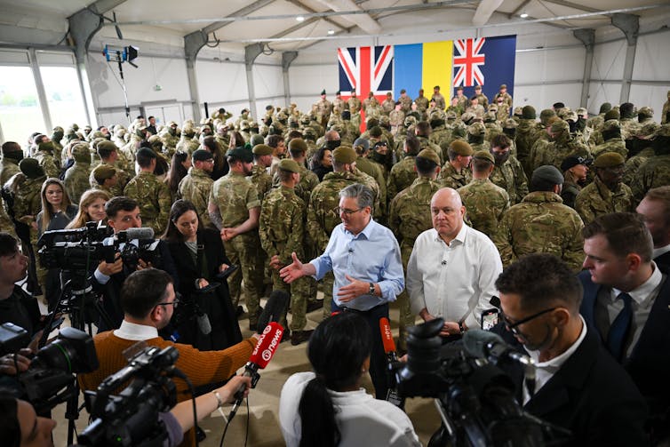 Keir Starmer and Christopher Luxon speak with media with British troops in background.