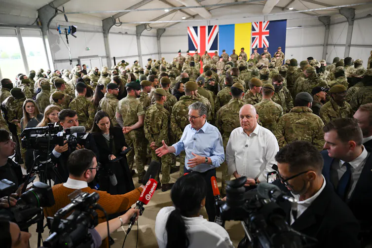 Keir Starmer and Christopher Luxon speak with media with British troops in background.