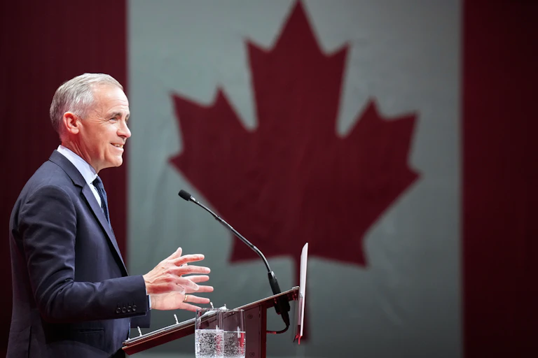 A man stands in front of a podium with a large Canadian flag beside him.