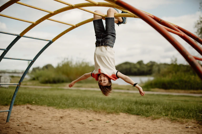 A happy child hangs upside down on monkey bars.