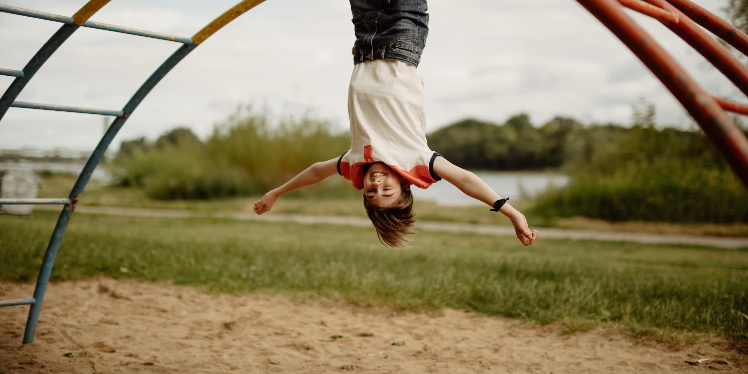 A happy child hangs upside down on monkey bars.