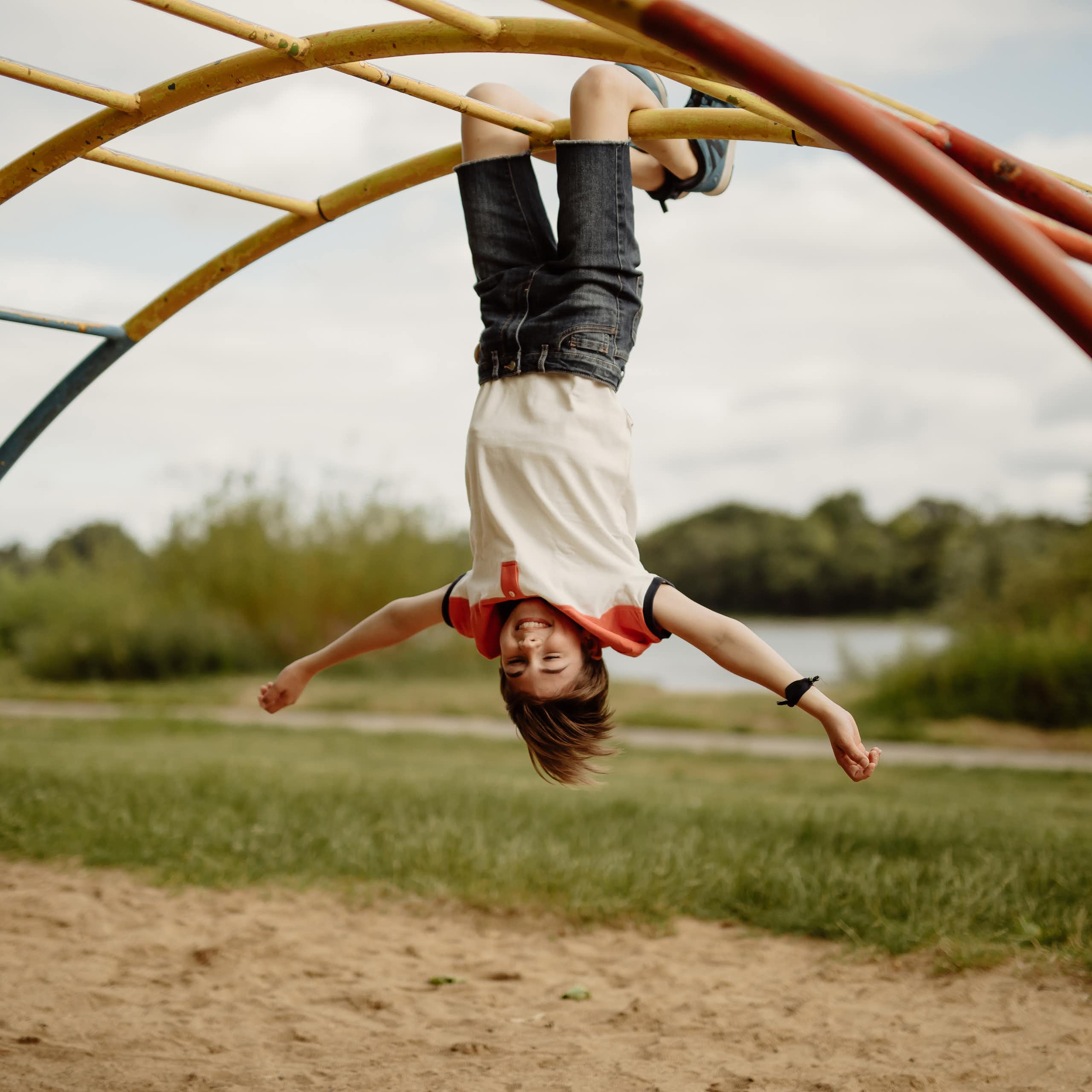 A happy child hangs upside down on monkey bars.