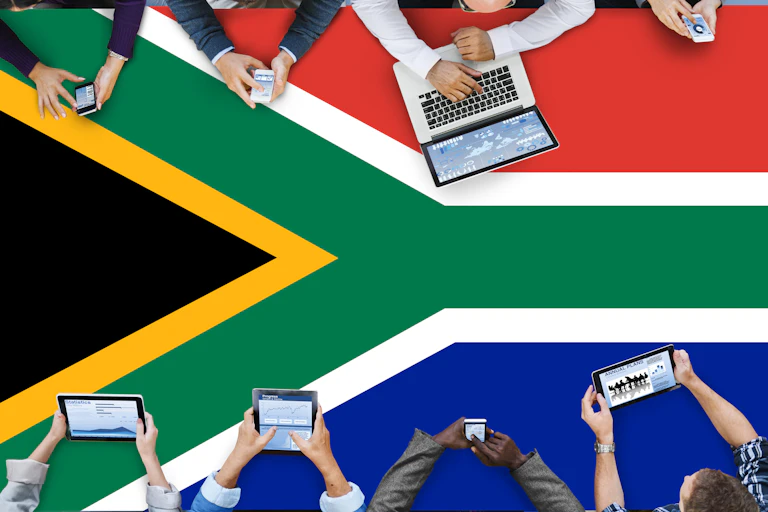 View from above of people using digital devices, on a surface representing the South African flag