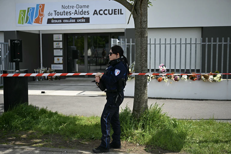 Une agente de la police municipale monte la garde devant le lycée Notre-Dame de Toutes-Aides, où des bouquets de fleurs et des messages ont été déposés, suite à l'attaque au couteau du 24 avril 2025, qui a fait un mort et trois blessés parmi les élèves, à Nantes.