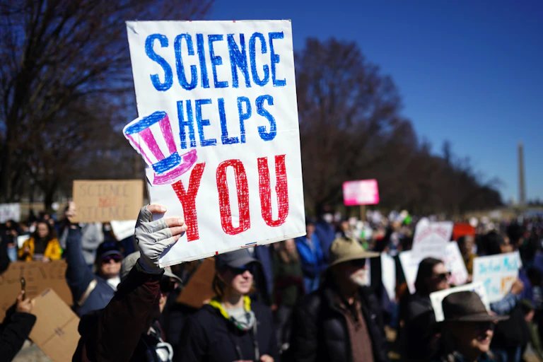 A sign saying science helps you held up by a protestor.
