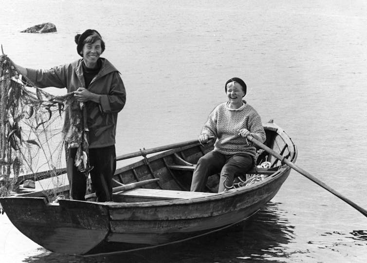 Two women in a boat casting off from a rocky island.