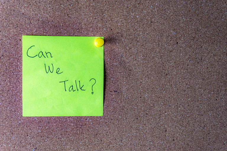 A green sticky note that says 'Can we talk?' is affixed to a board with a thumbtack.
