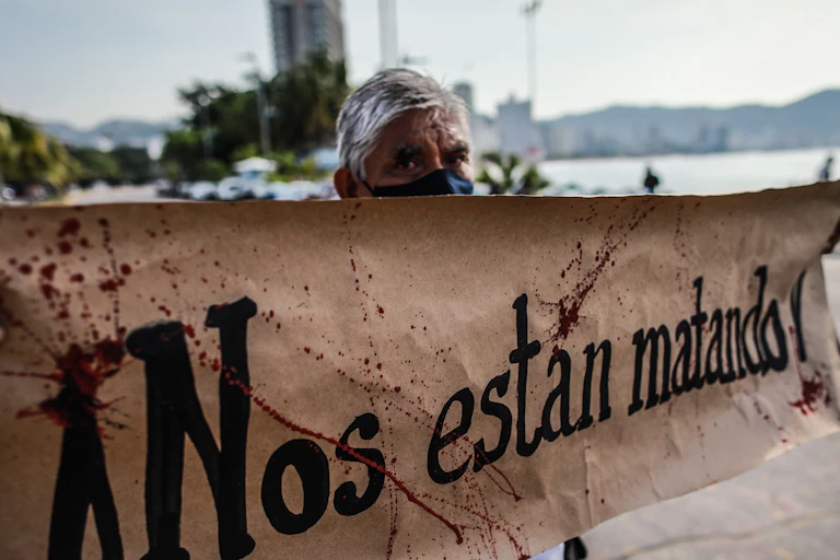 A grey-haired journalist protester holds up a sign in Spanish with blood-spattered effects, reading: 'They are killing us.'