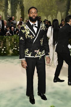 A man wearing an Black suit jacket with pink flowers and green vines.
