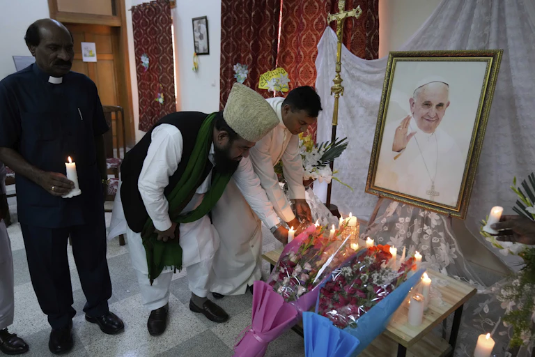 A Muslim cleric and a Christian priest place candles in front of the portrait of Pope Francis
