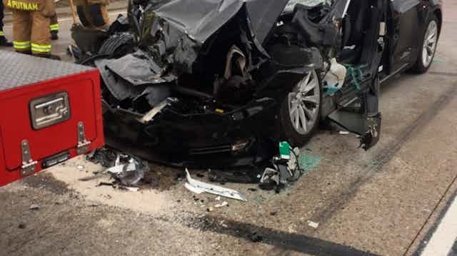 two firefighters stand near a sedan with a crumpled front end