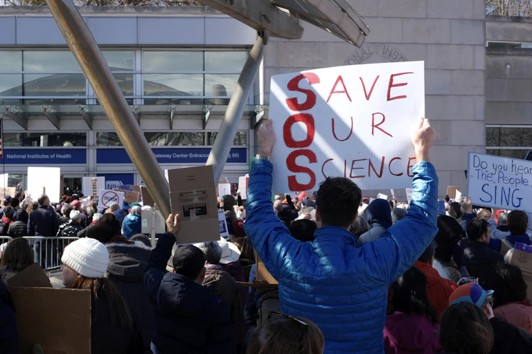 Demonstrators hold signs saying "Save Our Science" outside the NIH building