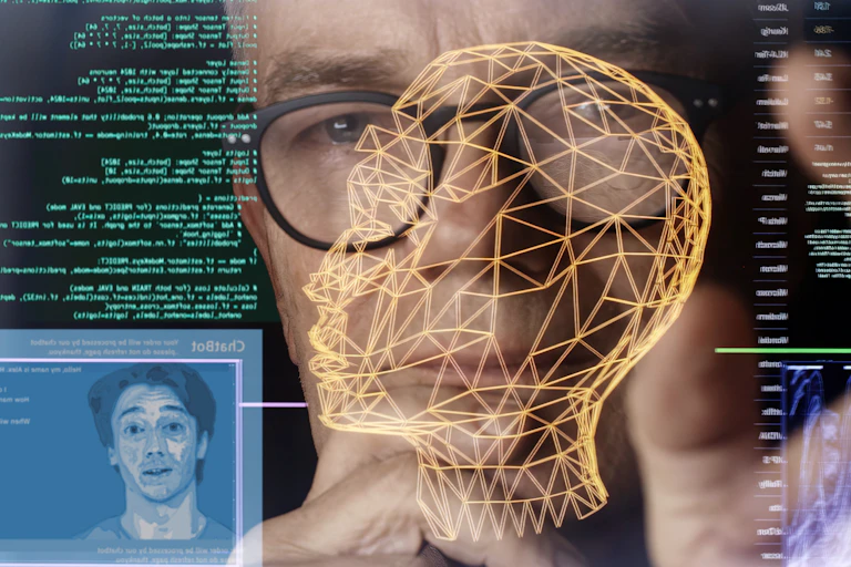Looking through a touch screen display to a man’s face. He’s studying imagery depicting AI (artificial intelligence) avatars, chatbots & associated coding.
