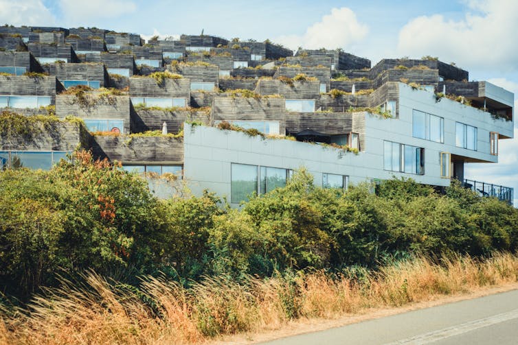 Rows of white and grey houses on a grassy rise next to a road